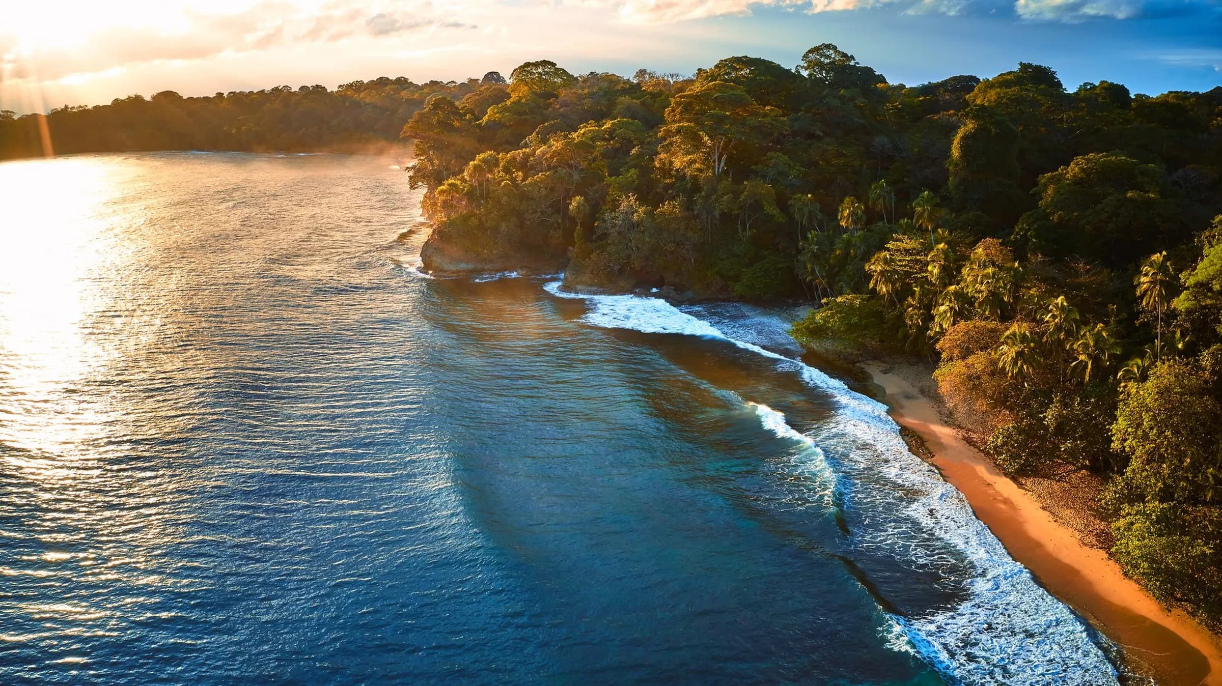 A golden-hour coastline of jungle, quiet surf and empty sand